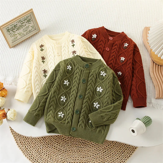 Three knitted sweaters in green, beige, and red on a textured surface.