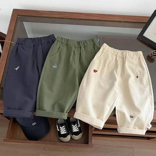 Three pairs of shorts in navy, green, and beige on a wooden surface with a small shoe.